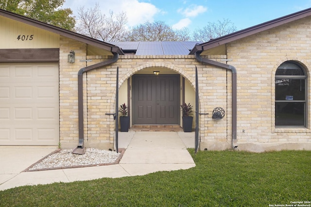 view of exterior entry with solar panels, a garage, and a lawn