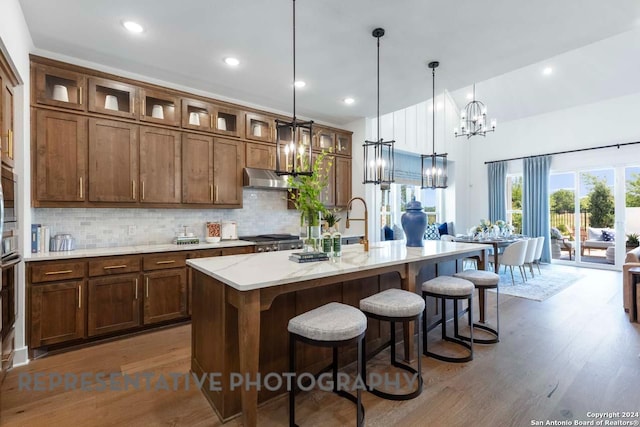 kitchen featuring light stone counters, an island with sink, dark wood-type flooring, and decorative light fixtures