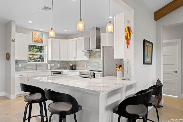 kitchen with kitchen peninsula, wall chimney exhaust hood, light stone countertops, white cabinetry, and stainless steel appliances