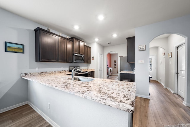 kitchen with arched walkways, a peninsula, a sink, dark brown cabinets, and stainless steel microwave