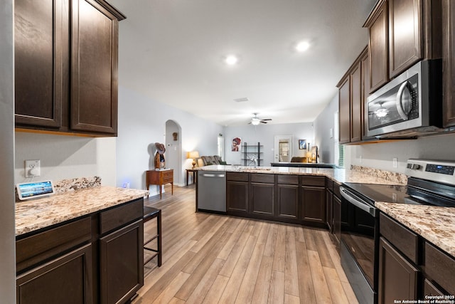 kitchen featuring light wood finished floors, arched walkways, appliances with stainless steel finishes, open floor plan, and a peninsula