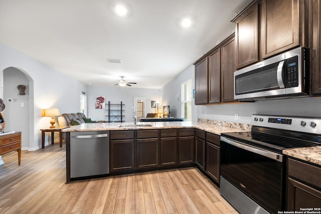 kitchen with appliances with stainless steel finishes, light wood-style floors, open floor plan, a sink, and a peninsula