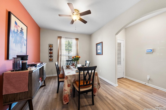 dining space featuring light wood finished floors, baseboards, arched walkways, and a ceiling fan