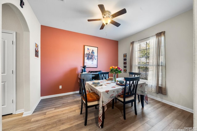 dining space featuring arched walkways, baseboards, and light wood finished floors