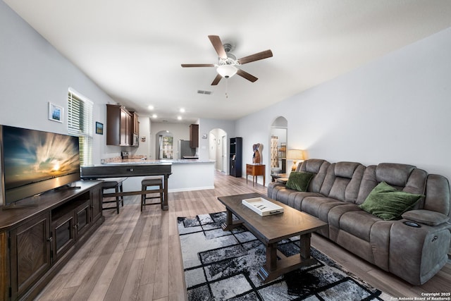 living area with light wood-type flooring, visible vents, arched walkways, and a ceiling fan