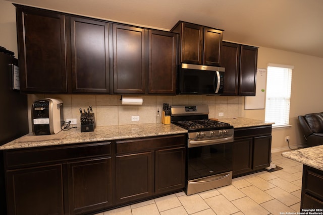 kitchen featuring dark brown cabinetry, light stone counters, light tile patterned flooring, and appliances with stainless steel finishes