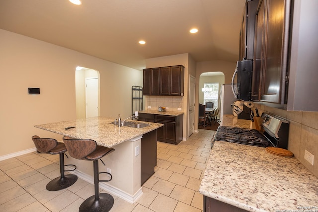 kitchen with light stone countertops, stainless steel range, sink, tasteful backsplash, and an island with sink