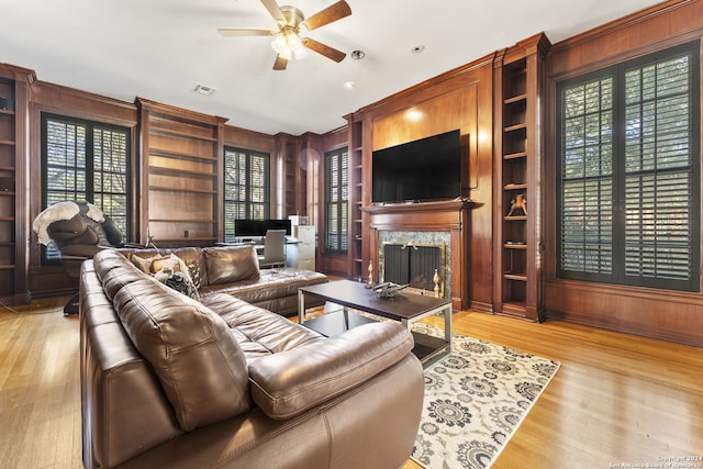 living room featuring built in shelves, a premium fireplace, ceiling fan, and wood walls