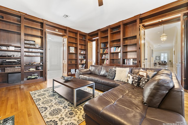 living room with hardwood / wood-style floors, built in shelves, crown molding, and ceiling fan with notable chandelier