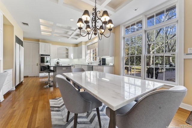 dining area featuring beam ceiling, sink, coffered ceiling, an inviting chandelier, and light wood-type flooring