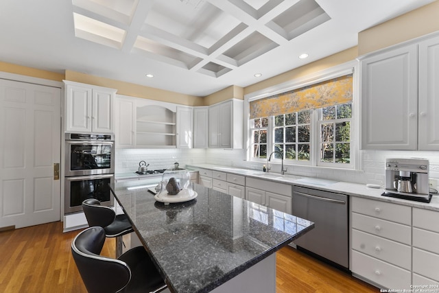 kitchen featuring coffered ceiling, stainless steel appliances, dark stone countertops, beamed ceiling, and a center island