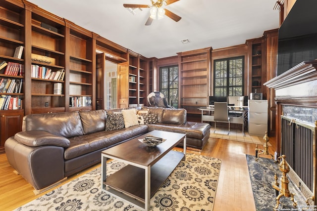 living room with light wood-type flooring, ceiling fan, built in features, a fireplace, and wood walls