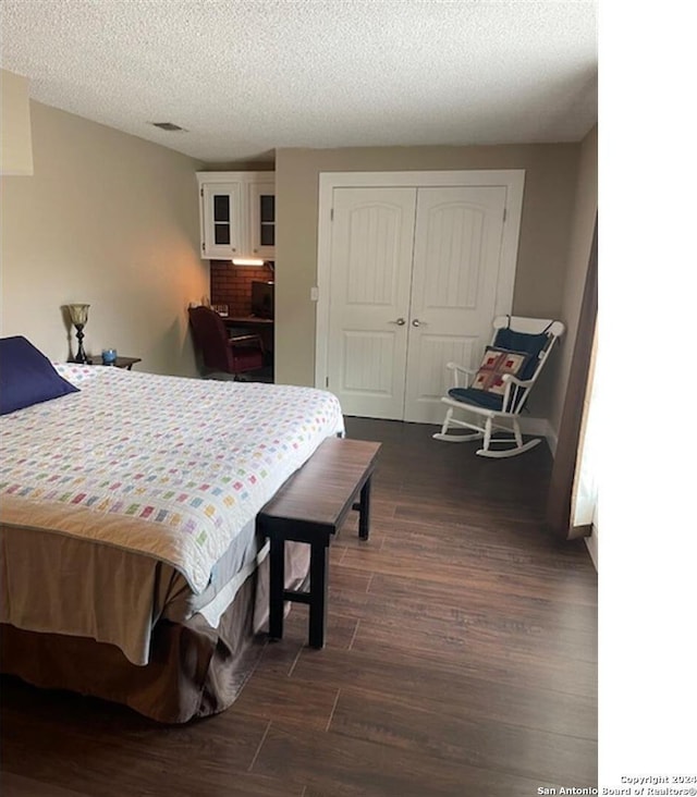 bedroom with a textured ceiling, dark wood-type flooring, and a closet