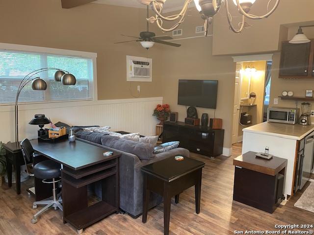 living room with ceiling fan with notable chandelier, wood-type flooring, and a wall unit AC