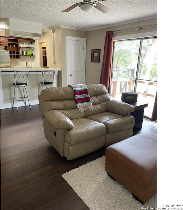 living room with ceiling fan, dark wood-type flooring, a textured ceiling, and ornamental molding