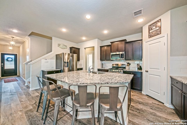 kitchen featuring sink, stainless steel appliances, light stone counters, an island with sink, and dark brown cabinets