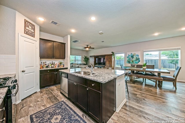 kitchen with sink, stainless steel appliances, decorative backsplash, a center island with sink, and dark brown cabinets