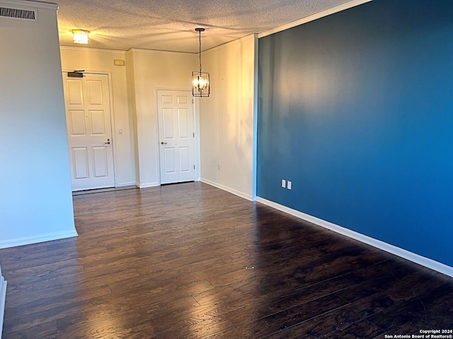 spare room with a textured ceiling, dark hardwood / wood-style flooring, an inviting chandelier, and crown molding