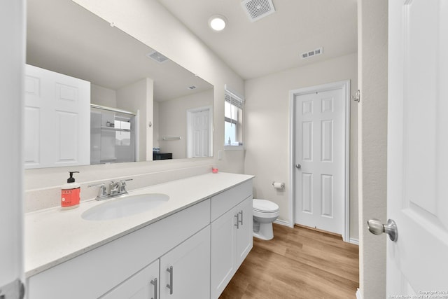 bathroom with hardwood / wood-style floors, vanity, a shower with door, and toilet