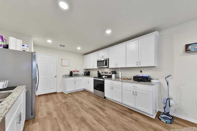 kitchen with light stone counters, white cabinets, stainless steel appliances, and light hardwood / wood-style floors