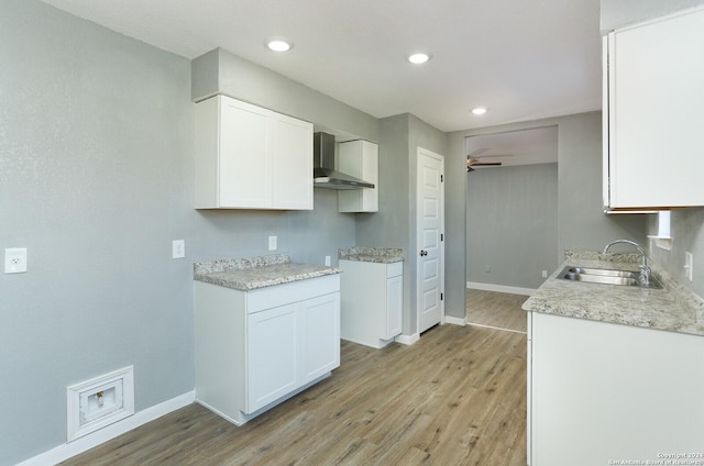 kitchen featuring white cabinetry, sink, ceiling fan, wall chimney range hood, and light hardwood / wood-style flooring