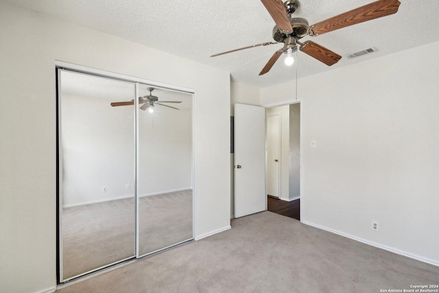 unfurnished bedroom with ceiling fan, a closet, light colored carpet, and a textured ceiling