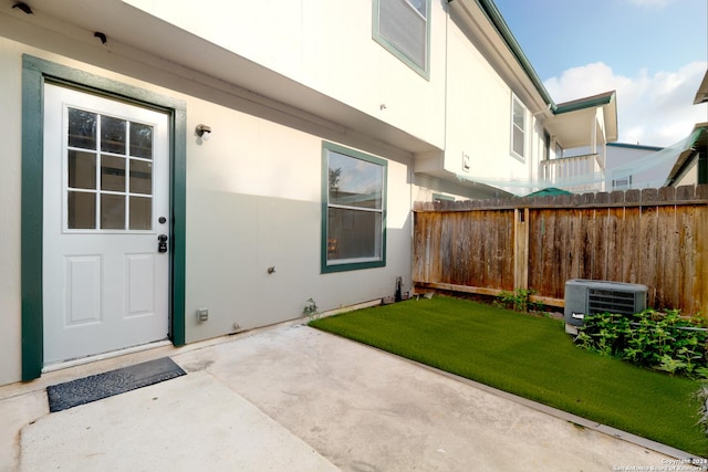 view of exterior entry featuring a lawn, cooling unit, and a patio