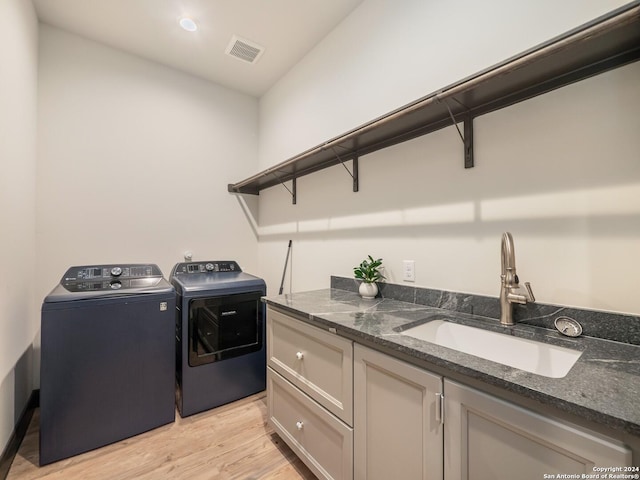 clothes washing area featuring washing machine and clothes dryer, sink, cabinets, and light hardwood / wood-style flooring