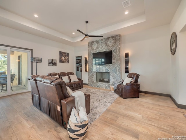 living room with a tray ceiling, a premium fireplace, ceiling fan, and light hardwood / wood-style floors