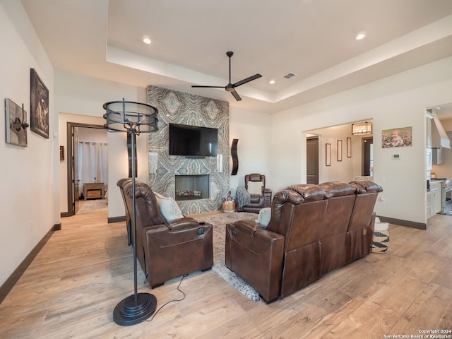 living room featuring a tray ceiling, a fireplace, and light wood-type flooring