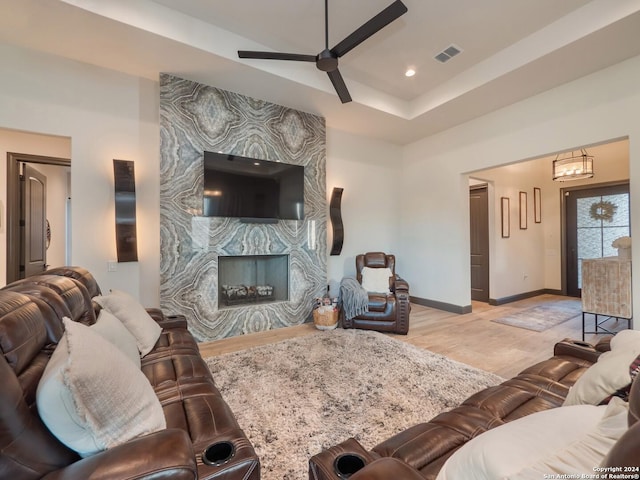 living room with ceiling fan, a raised ceiling, a fireplace, and light hardwood / wood-style flooring