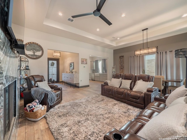 living room featuring a fireplace, light wood-type flooring, a raised ceiling, and ceiling fan