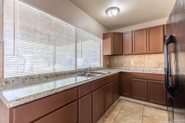 kitchen featuring light stone countertops, black fridge, sink, light tile patterned floors, and lofted ceiling