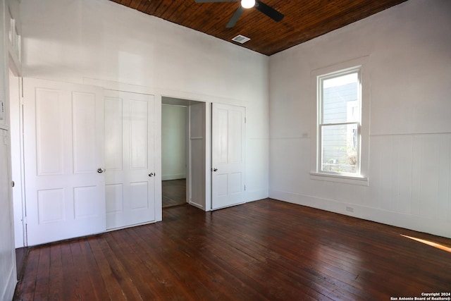 unfurnished bedroom featuring ceiling fan, wood ceiling, dark wood-type flooring, and two closets