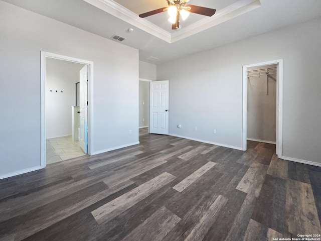 unfurnished bedroom featuring dark hardwood / wood-style flooring, ensuite bathroom, a tray ceiling, ceiling fan, and a closet