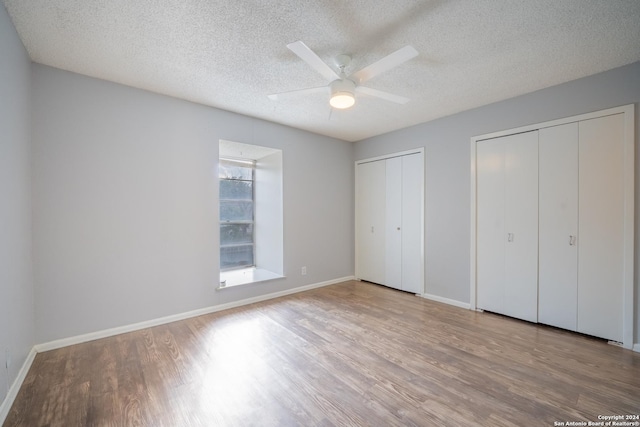 unfurnished bedroom with a textured ceiling, light hardwood / wood-style flooring, ceiling fan, and multiple closets