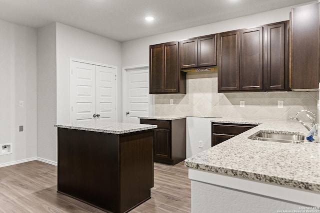 2659 Greenwell Ln, New Braunfels, TX 78130 - kitchen with dark brown cabinets, light stone countertops, a kitchen island, light wood-type flooring, and backsplash