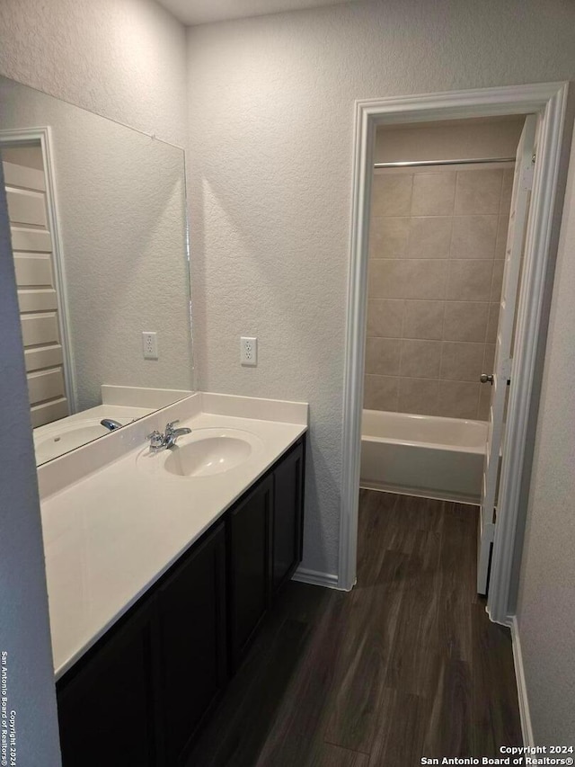 bathroom with hardwood / wood-style floors, vanity, and tiled shower / bath