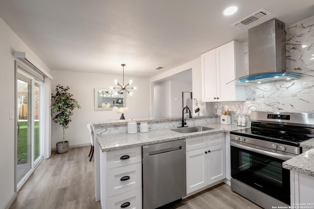 kitchen with kitchen peninsula, appliances with stainless steel finishes, wall chimney exhaust hood, sink, and white cabinets