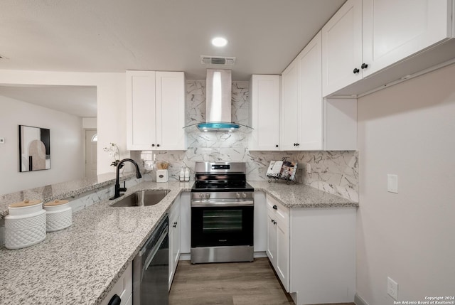 kitchen featuring light stone countertops, stainless steel appliances, sink, wall chimney range hood, and white cabinetry