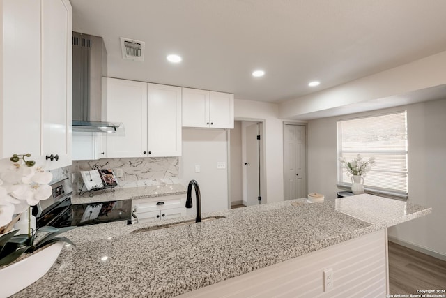 kitchen featuring light stone countertops, tasteful backsplash, wall chimney range hood, range, and white cabinetry