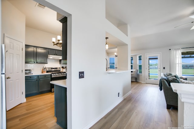 kitchen with backsplash, stainless steel gas range, ceiling fan with notable chandelier, pendant lighting, and light hardwood / wood-style flooring