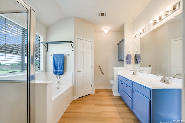 bathroom with a washtub, vanity, vaulted ceiling, hardwood / wood-style flooring, and toilet