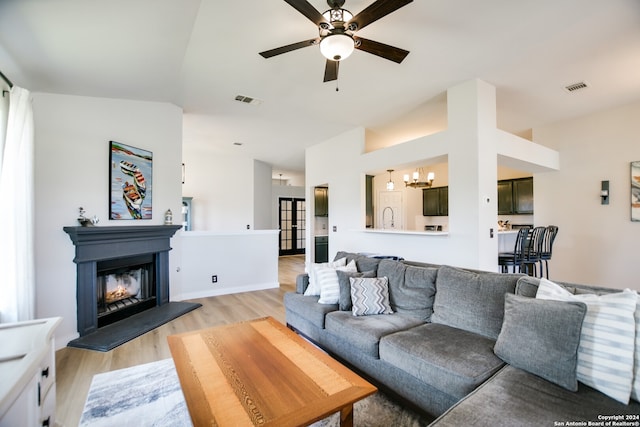 living room with ceiling fan with notable chandelier, light hardwood / wood-style floors, and lofted ceiling