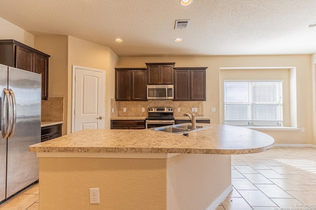 kitchen featuring tasteful backsplash, stainless steel appliances, sink, light tile patterned floors, and a center island with sink