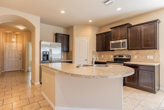 kitchen featuring decorative backsplash, appliances with stainless steel finishes, sink, and an island with sink