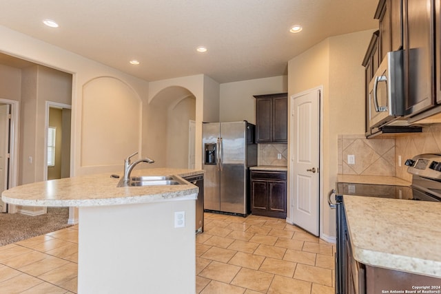 kitchen featuring a kitchen island with sink, sink, light tile patterned floors, appliances with stainless steel finishes, and tasteful backsplash