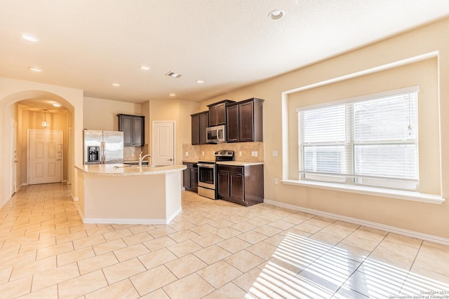 kitchen with a center island with sink, light stone countertops, light tile patterned floors, appliances with stainless steel finishes, and tasteful backsplash