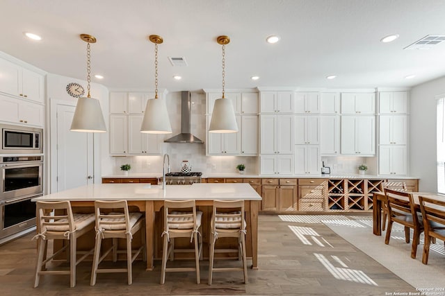 kitchen with white cabinetry, a kitchen island with sink, and wall chimney range hood