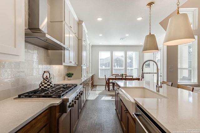 kitchen featuring backsplash, sink, hanging light fixtures, wall chimney exhaust hood, and stainless steel appliances